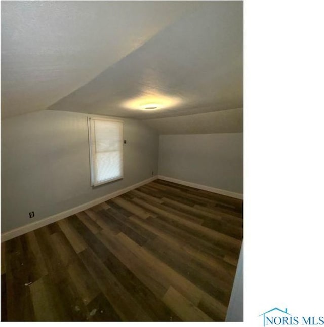additional living space with baseboards, vaulted ceiling, and dark wood-style floors
