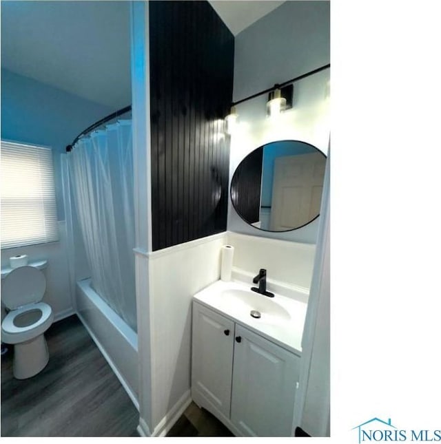bathroom featuring toilet, shower / bath combo with shower curtain, wood finished floors, and vanity