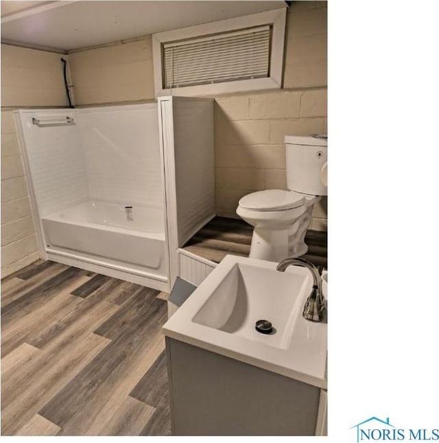 full bathroom with concrete block wall, vanity, toilet, and wood finished floors