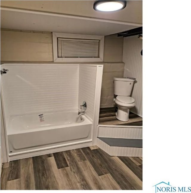 full bath featuring toilet, a tub to relax in, and wood finished floors