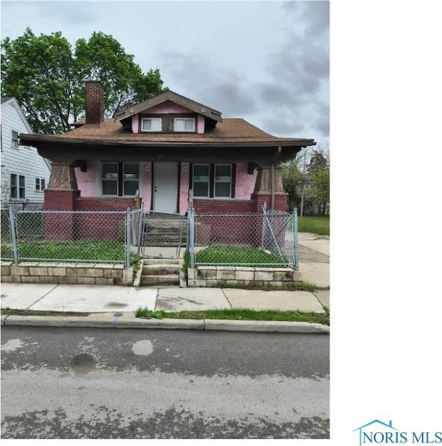 bungalow-style home with covered porch, a chimney, brick siding, a gate, and a fenced front yard