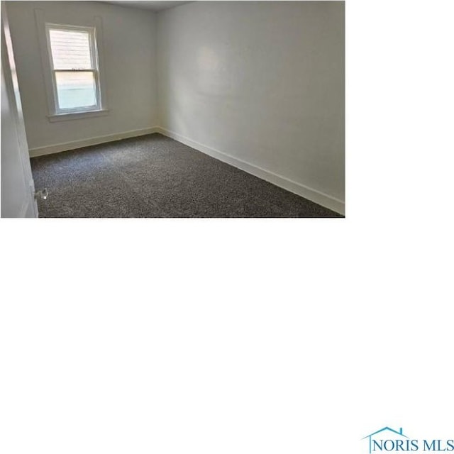 spare room featuring baseboards and dark carpet