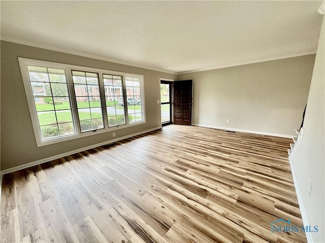 empty room featuring baseboards, ornamental molding, wood finished floors, and stairway