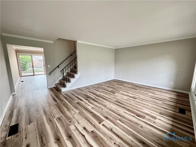 unfurnished living room featuring visible vents, wood finished floors, stairway, baseboards, and ornamental molding