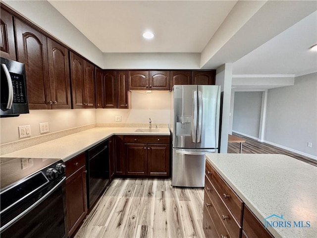 kitchen featuring light countertops, light wood finished floors, dark brown cabinetry, and black appliances