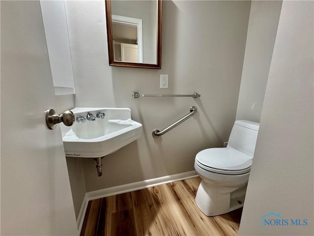bathroom featuring baseboards, a sink, wood finished floors, and toilet