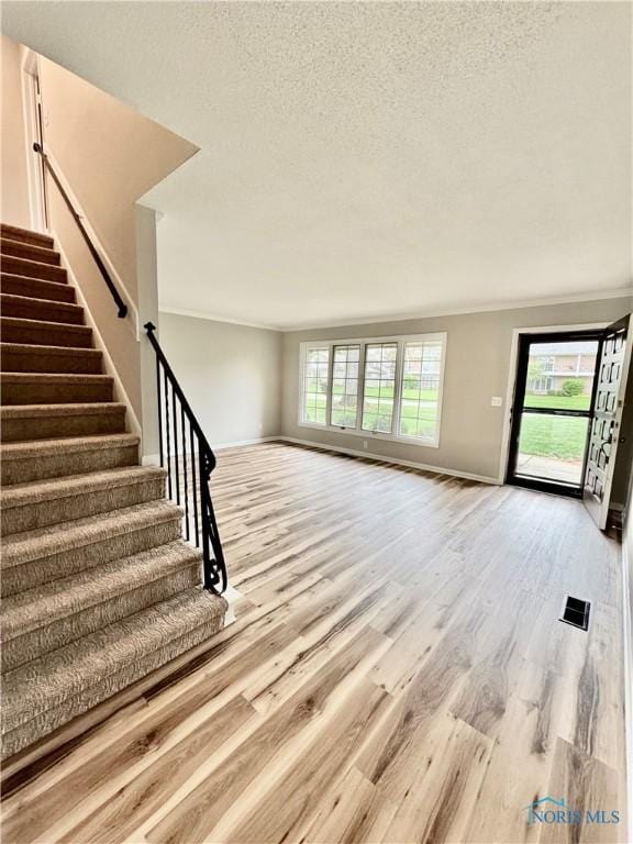 unfurnished living room featuring light wood finished floors, a textured ceiling, stairs, baseboards, and visible vents