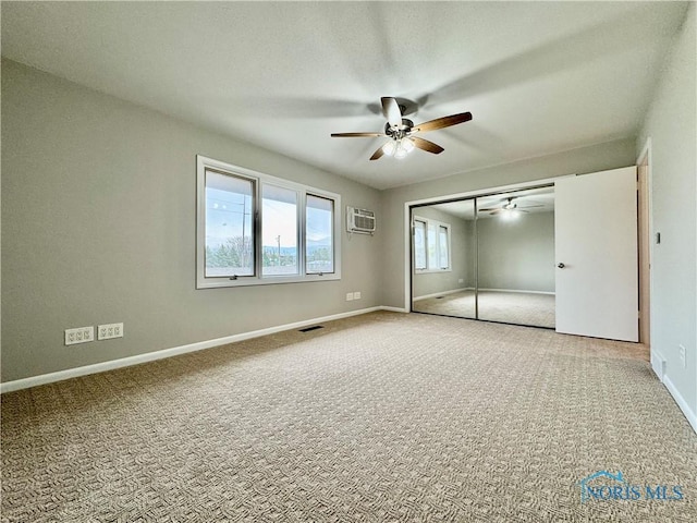 unfurnished bedroom with an AC wall unit, baseboards, carpet, and a closet