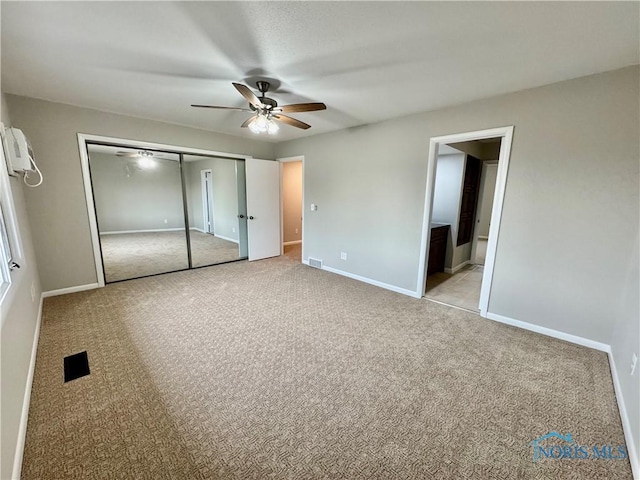 unfurnished bedroom featuring light colored carpet, a wall mounted AC, visible vents, and a closet