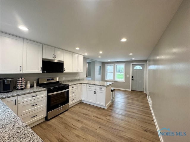 kitchen with white cabinetry, a peninsula, stainless steel appliances, recessed lighting, and light wood-style flooring