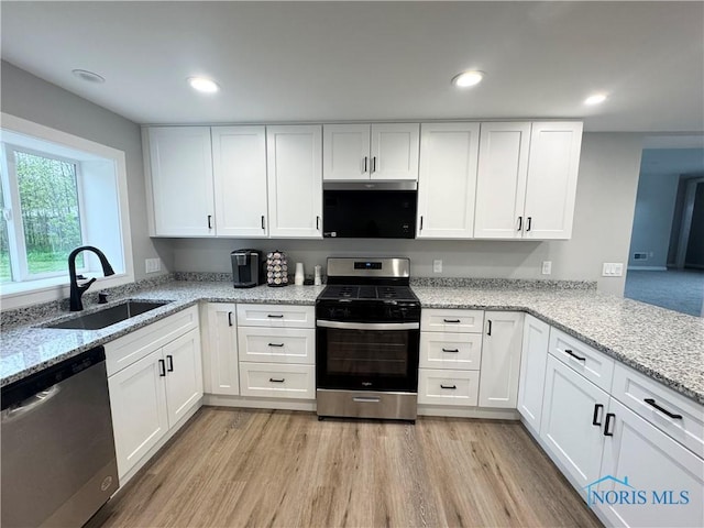 kitchen with white cabinets, stainless steel appliances, light stone countertops, and a sink