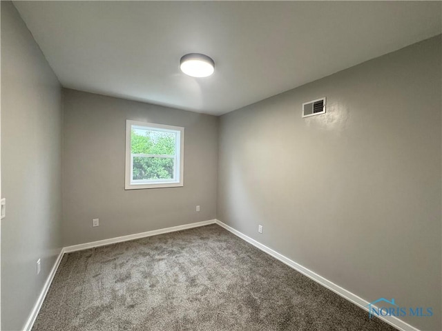empty room with baseboards, visible vents, and dark colored carpet