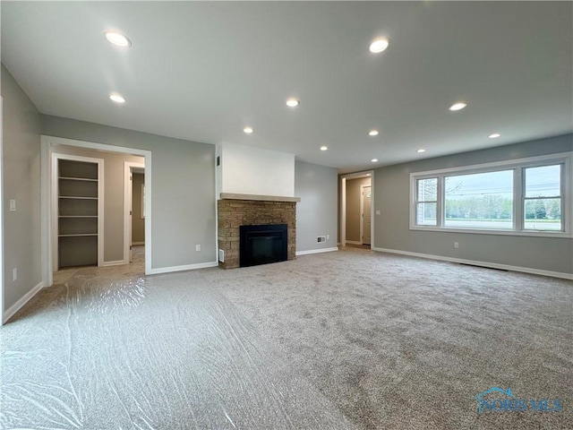 unfurnished living room featuring baseboards, recessed lighting, a stone fireplace, and light colored carpet