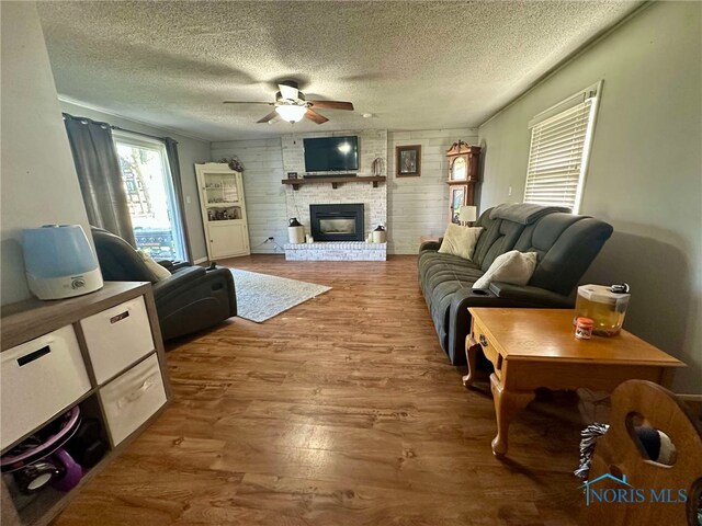 living area with a brick fireplace, a textured ceiling, ceiling fan, and wood finished floors