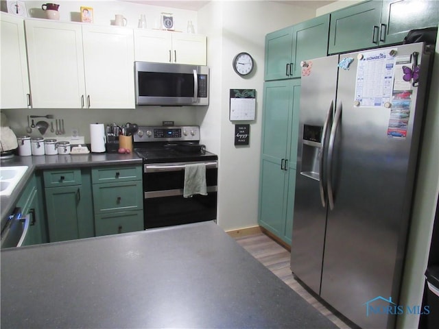 kitchen featuring green cabinetry, dark countertops, stainless steel appliances, and light wood-style flooring