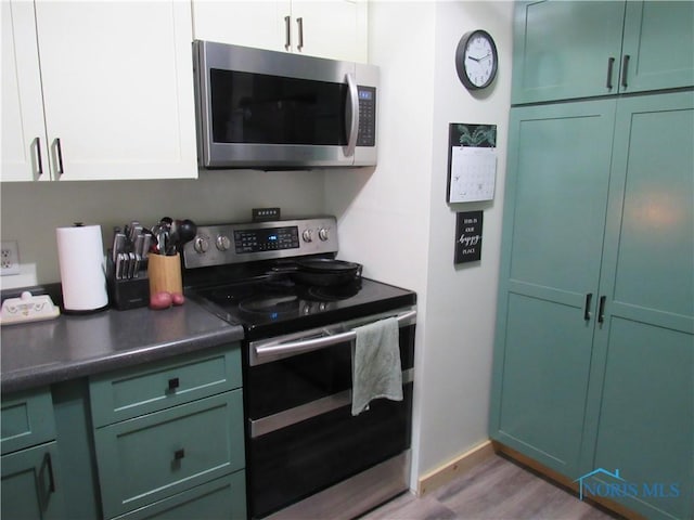 kitchen with baseboards, light wood finished floors, green cabinetry, dark countertops, and appliances with stainless steel finishes