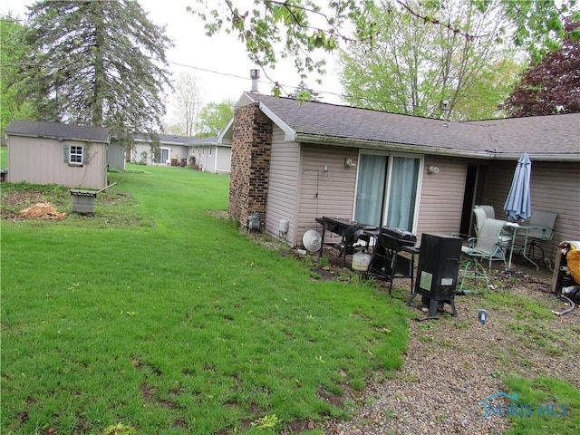 back of house with a yard, a shingled roof, and an outbuilding