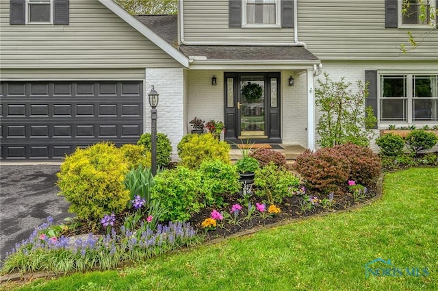 doorway to property with a lawn, a shingled roof, a garage, and brick siding