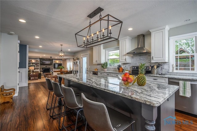 kitchen with open floor plan, dishwasher, dark wood-style floors, and wall chimney range hood