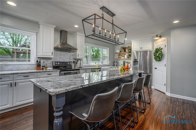 kitchen featuring white cabinets, light stone countertops, wall chimney exhaust hood, stainless steel appliances, and backsplash