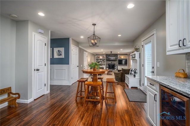 dining area with a fireplace, a wainscoted wall, beverage cooler, recessed lighting, and dark wood-type flooring