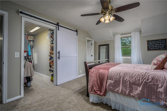 carpeted bedroom with a walk in closet, ceiling fan, vaulted ceiling, a barn door, and baseboards