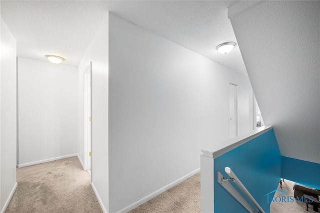 hallway with carpet floors, baseboards, and an upstairs landing