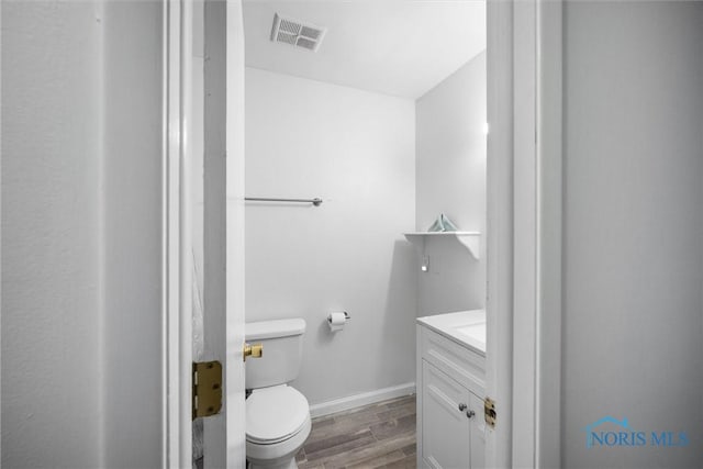 bathroom featuring vanity, toilet, baseboards, wood finished floors, and visible vents