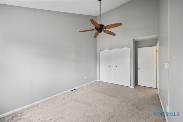 unfurnished bedroom with baseboards, carpet flooring, a closet, and high vaulted ceiling