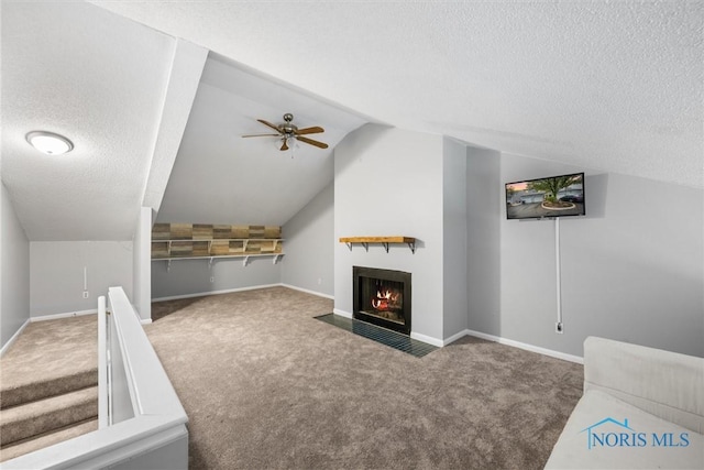 unfurnished living room featuring carpet floors, a textured ceiling, a ceiling fan, a fireplace with flush hearth, and lofted ceiling