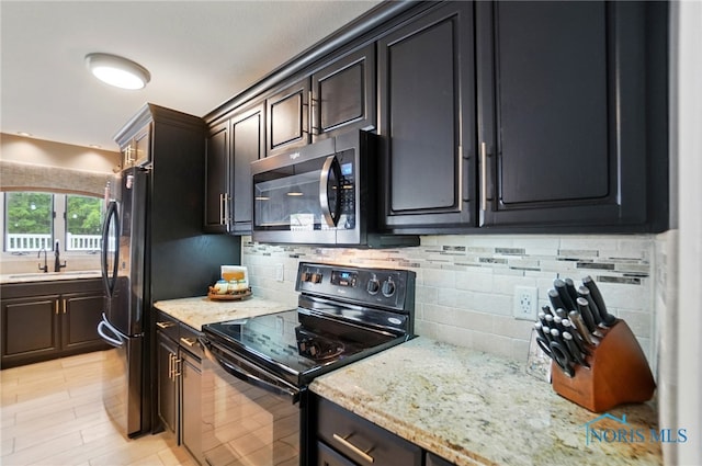 kitchen with a sink, light stone counters, backsplash, and black appliances