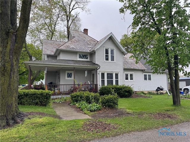 view of front facade featuring covered porch, a chimney, and a front yard
