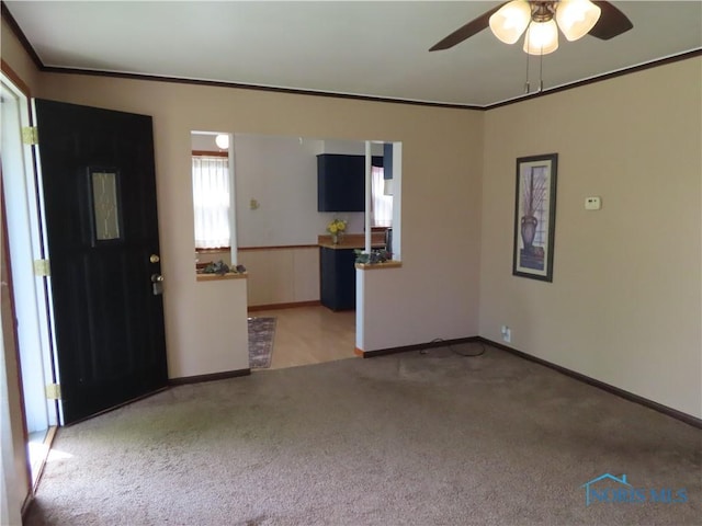 interior space featuring light colored carpet, baseboards, a ceiling fan, and ornamental molding