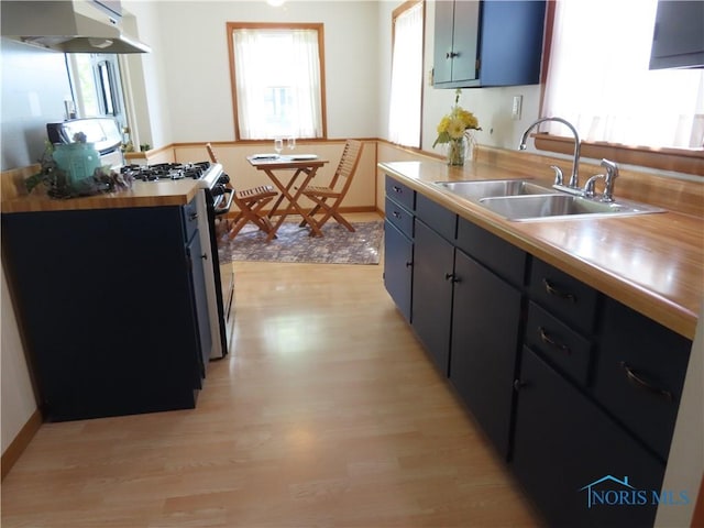 kitchen featuring light wood finished floors, a sink, wood counters, stainless steel range with gas stovetop, and under cabinet range hood
