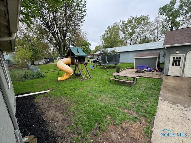 view of playground featuring a storage shed, a trampoline, fence, a lawn, and an outdoor structure