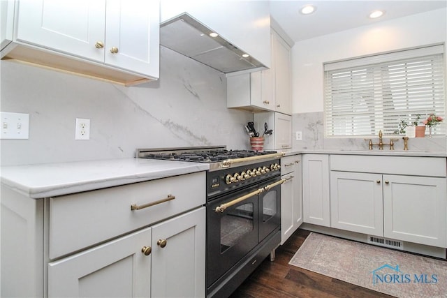 kitchen with visible vents, wall chimney exhaust hood, light countertops, range with two ovens, and dark wood-style floors