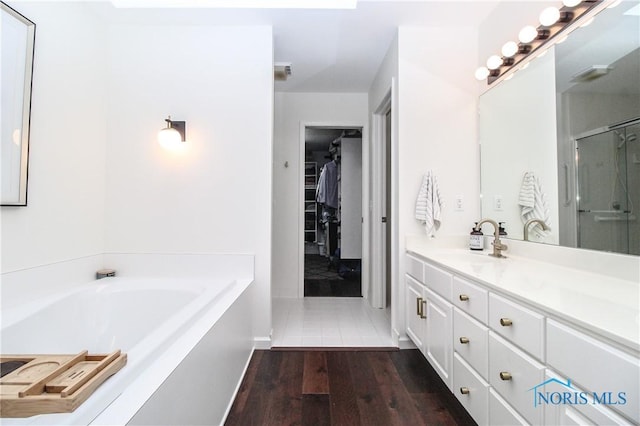 full bath with a shower with door, a garden tub, vanity, wood finished floors, and a spacious closet