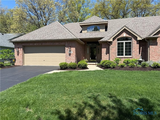 view of front of property with an attached garage, aphalt driveway, a front lawn, brick siding, and roof with shingles