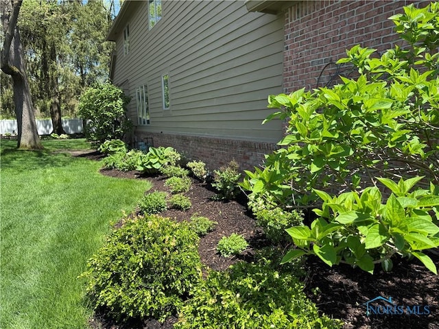 view of side of property with a lawn, brick siding, and fence
