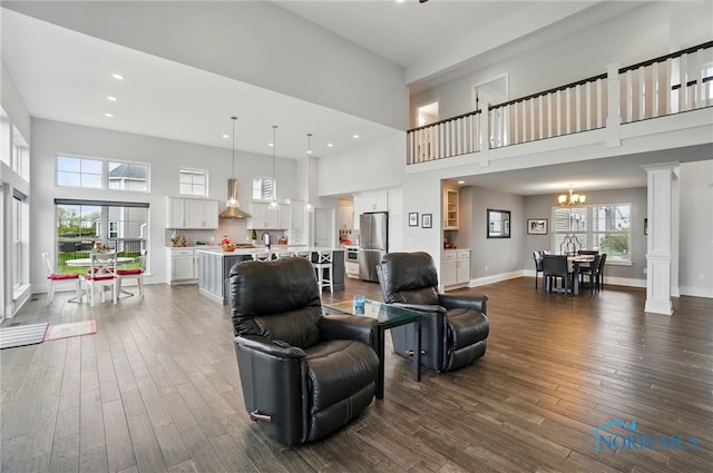 living area with a towering ceiling, dark wood-style flooring, a chandelier, decorative columns, and plenty of natural light