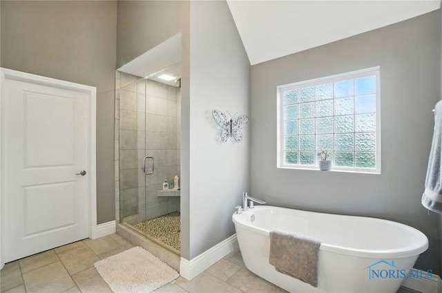bathroom with a stall shower, vaulted ceiling, a freestanding tub, baseboards, and tile patterned floors