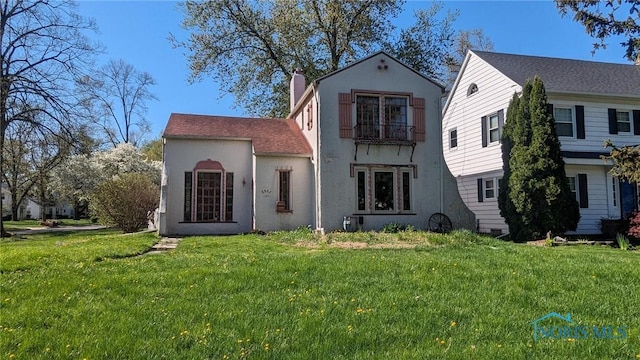 view of front of home with a front yard, stucco siding, a chimney, and a balcony