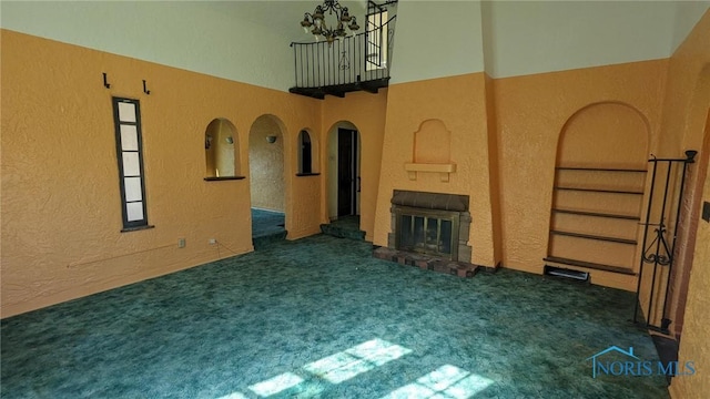 unfurnished living room with a textured wall, carpet, a notable chandelier, and a glass covered fireplace