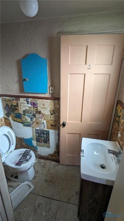 half bathroom with toilet, marble finish floor, vanity, and a textured wall