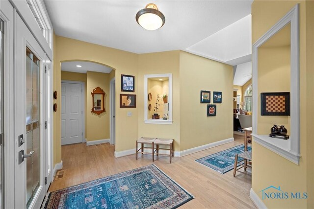 hallway with visible vents, wood finished floors, baseboards, and arched walkways