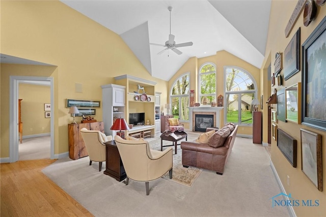 living area featuring high vaulted ceiling, light wood-style flooring, a ceiling fan, baseboards, and a tiled fireplace