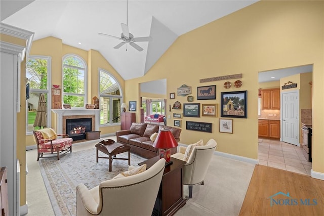 living area with light colored carpet, high vaulted ceiling, a ceiling fan, baseboards, and a glass covered fireplace