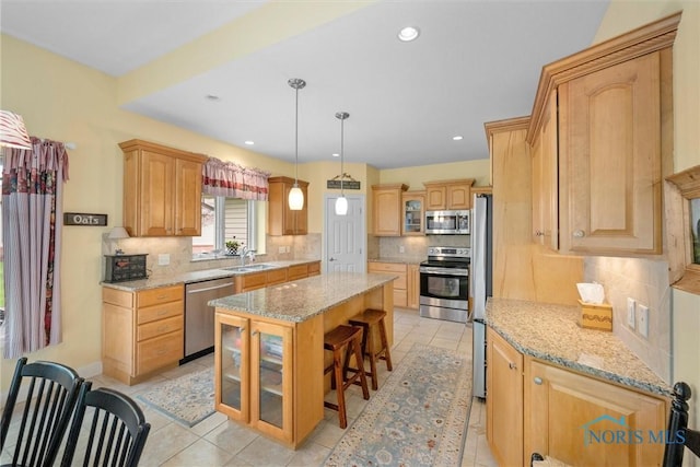 kitchen with a kitchen bar, a sink, backsplash, appliances with stainless steel finishes, and a kitchen island