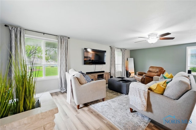 living room featuring baseboards, light wood-style flooring, and ceiling fan