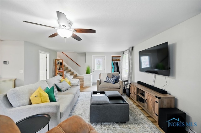 living area featuring stairs, baseboard heating, ceiling fan, and wood finished floors